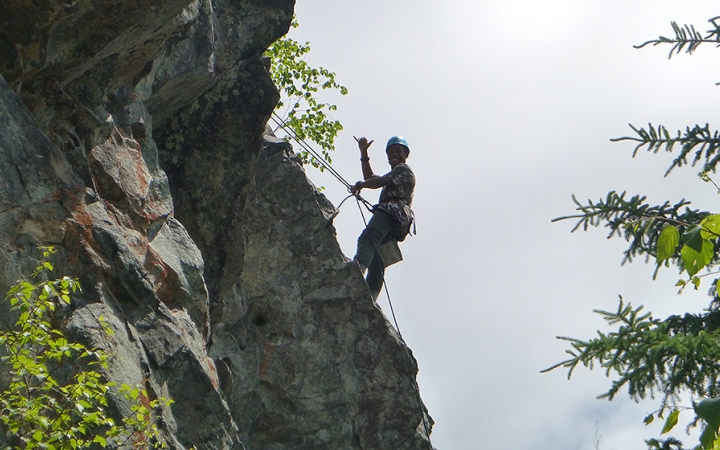a person gives the hang loose sign with a free hand while rock climbing 